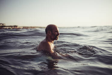 Älterer Mann schwimmt bei Sonnenuntergang im Meer - MEUF02067