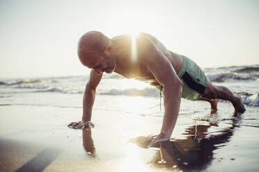 Älterer Mann trainiert am Strand bei Sonnenuntergang - MEUF02071