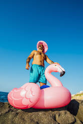 Mann mit Hut steht auf Flamingo-Ring gegen klaren Himmel - MEUF02090