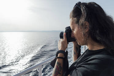 Frau, die durch eine Kamera fotografiert, während sie auf einem Passagierschiff steht - MEUF02094