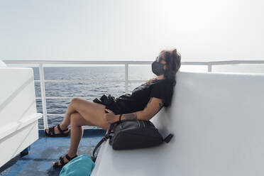Woman wearing face mask resting while sitting in passenger craft - MEUF02095