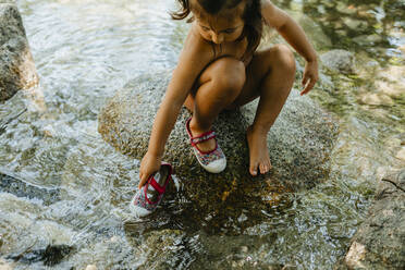 Nettes Mädchen spielt im fließenden Wasser, während es im Sommer auf einem Felsen sitzt - VABF03470