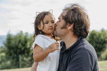 Father kissing daughter while sitting at back yard - VABF03474