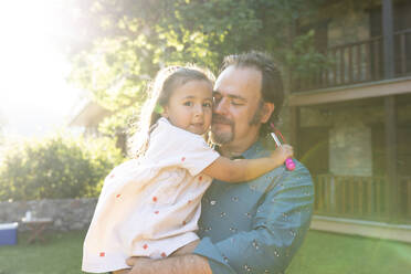 Father holding daughter while standing at backyard - VABF03495