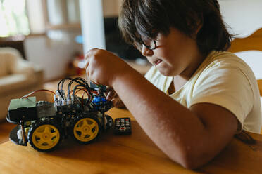 Boy repairing remote controlled car while sitting by table at home - VABF03498