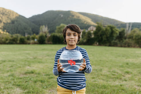 Lächelnder Junge hält ein Fischglas in der Hand, während er im Hinterhof steht - VABF03501