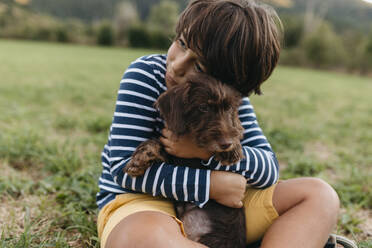 Boy embracing puppy while sitting on grass at backyard - VABF03506