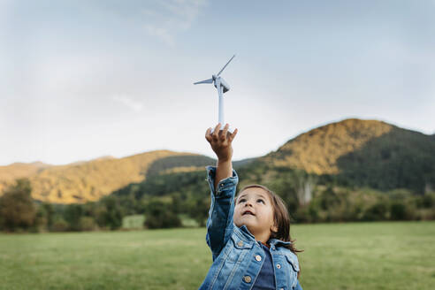 Cute girl playing with wind turbine toy while standing at backyard - VABF03510