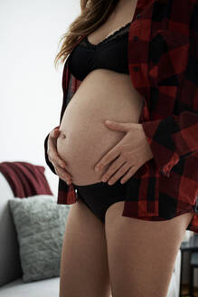 Close-up of pregnant woman touching stomach while standing at home - BZF00575