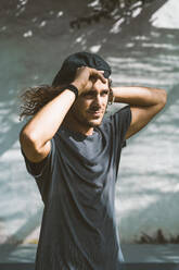 Young man wearing cap looking away while standing against white wall - DAMF00460