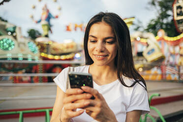 Nahaufnahme einer schönen Frau, die in einem Vergnügungspark ein Mobiltelefon benutzt - OYF00199