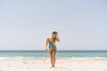 Frau mit Bodysuit und Sonnenbrille beim Spaziergang am Strand von Valdevaqueros, Tarifa, Spanien - DAMF00462