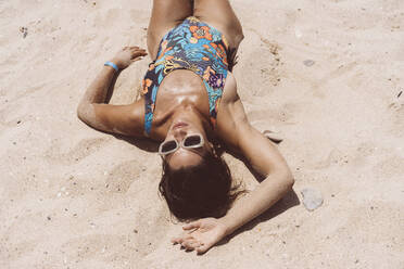 Mid adult woman wearing bodysuit lying at Valdevaqueros beach on sunny day, Tarifa, Spanien - DAMF00464