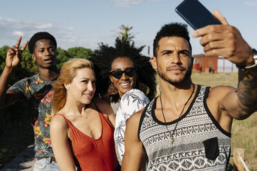 Lächelnde Freunde, die ein Selfie mit ihrem Smartphone machen, während sie in einem öffentlichen Park stehen - RDGF00136