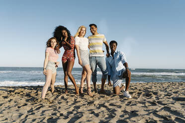 Junge Freunde stehen an einem sonnigen Tag im Sand am Wasser - RDGF00155