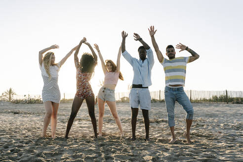 Freunde mit erhobener Hand am Strand stehend an einem sonnigen Tag - RDGF00162