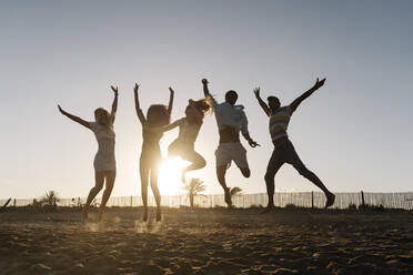 Freunde springen vor Freude am Strand bei Sonnenuntergang - RDGF00163