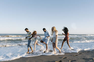 Junge Freunde spielen im Wasser am Strand an einem sonnigen Tag - RDGF00164