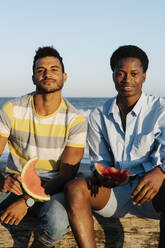 Freunde essen Wassermelone am Strand sitzend - RDGF00174