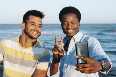 Smiling friends taking selfie on smart phone at beach during sunny day - RDGF00177