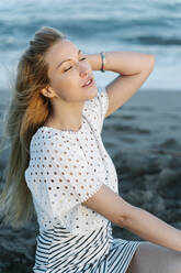 Junge Frau mit Hand im Haar am Strand sitzend - RDGF00190