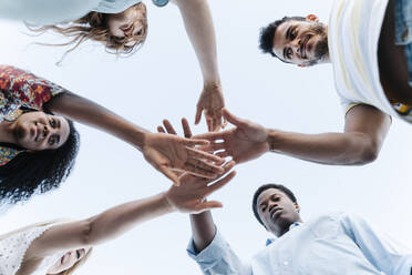 Low angle view of friends bring their hands together in show of unity before playing game - RDGF00199