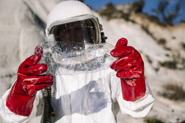 Nahaufnahme eines männlichen Astronauten, der eine Plastikflasche hält, während er auf einem anderen Planeten steht - JCMF01435