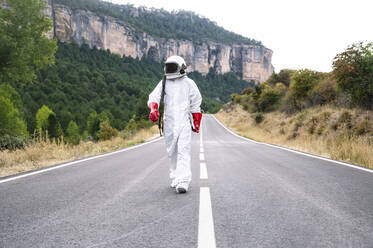 Männlicher Astronaut im Raumanzug, der auf einer Straße gegen einen Berg läuft - JCMF01439