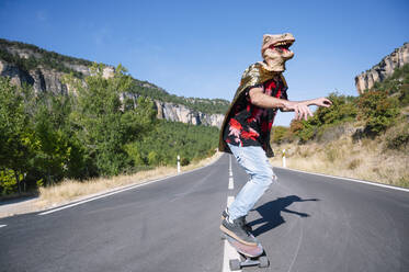 Mann mit Dinosaurier-Maske fährt mit dem Skateboard auf der Straße gegen den klaren Himmel - PGF00017