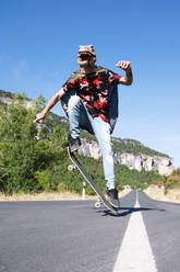 Mann mit Dinosauriermaske und Umhang fährt Skateboard auf der Straße gegen den klaren Himmel - PGF00018