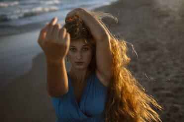 Junge Frau mit Hand im Haar tanzt am Strand - GMLF00619