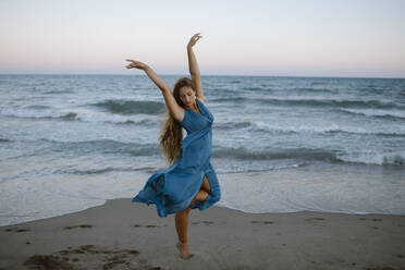 Young woman dancing against sea at beach - GMLF00627