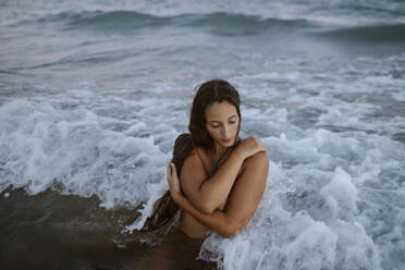 Woman with arms crossed taking bath in water at beach - GMLF00634