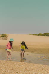 Sisters fishing crabs in sea while standing against clear sky during sunny day - ERRF04414