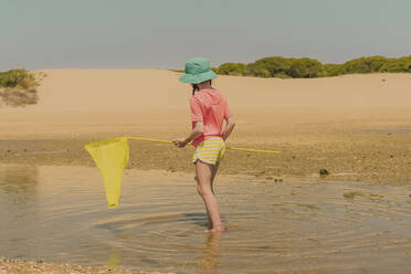 Mädchen, das ein gelbes Fischernetz hält, während es im Meer vor einem klaren Himmel steht - ERRF04418
