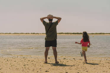 Vater mit Tochter stehen am Strand gegen den klaren Himmel an einem sonnigen Tag - ERRF04422