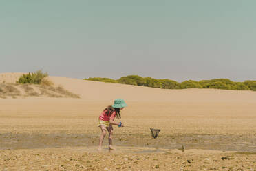 Girl fishing crab at beach against clear sky during sunny day - ERRF04425