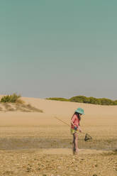 Girl wearing hat fishing crab at beach against clear sky during sunny day - ERRF04426