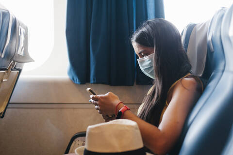 Woman wearing mask using smart phone while sitting on seat in cruise ship stock photo