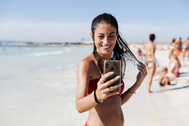 Smiling woman wearing bikini taking selfie with mobile phone at beach against sky - EGAF00756