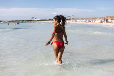 Happy woman wearing bikini walking in sea against sky - EGAF00757