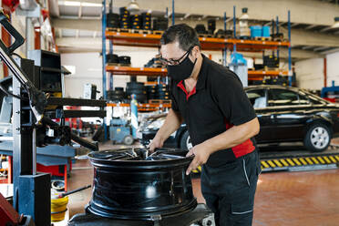 Mechaniker mit Maske bei der Arbeit in einer Autowerkstatt - EGAF00764