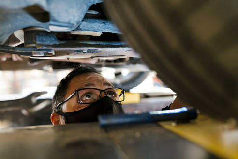 Nahaufnahme eines Mechanikers mit Maske, der ein Auto in einer Autowerkstatt untersucht - EGAF00767