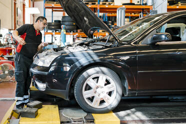 Male mechanic repairing car while standing in auto repair shop - EGAF00774