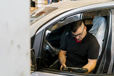 Mechaniker untersucht Auto, während er auf dem Fahrzeugsitz in der Garage sitzt - EGAF00779