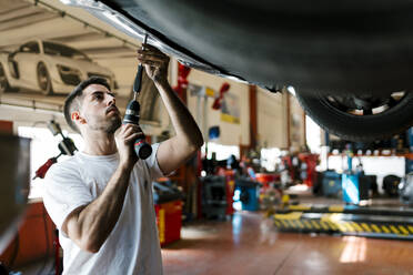 Junger Mechaniker repariert Auto mit Arbeitswerkzeug in einer Autowerkstatt - EGAF00781