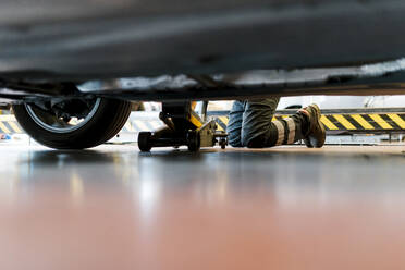 Mechanic changing tire while kneeling on floor in auto repair shop - EGAF00783