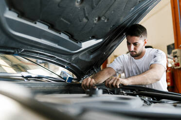 Young man repairing car while standing in auto repair shop - EGAF00786