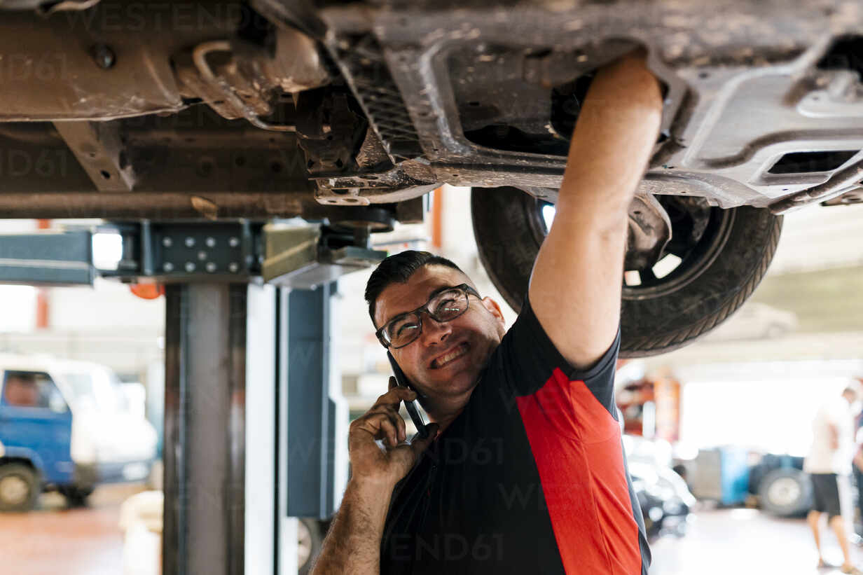 Mechanic talking over mobile phone while repairing car in workshop stock  photo