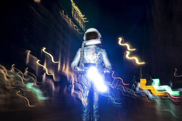 Male astronaut wearing space suit standing amidst light paintings on street at night - JCMF01446